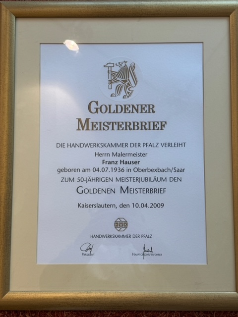 Innenansicht einer Lagerhalle mit mehreren Regalen, die mit Baumaterialien bestückt sind. Es gibt Säcke mit Beschriftungen, Eimer, Werkzeuge und diverse andere Bauartikel. Die Regale sind in verschiedenen Farben, darunter Gelb und Blau. Der Boden der Halle ist betoniert und mit gelben Markierungen versehen. Das Dach besteht aus Metallträgern, und es gibt mehrere Beleuchtungskörper, die die Halle erhellen.